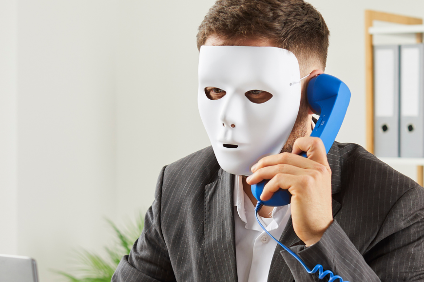 A professional wearing a white mask while speaking on a blue phone, symbolizing the concept of hiring scams and fraudulent activity on LinkedIn.