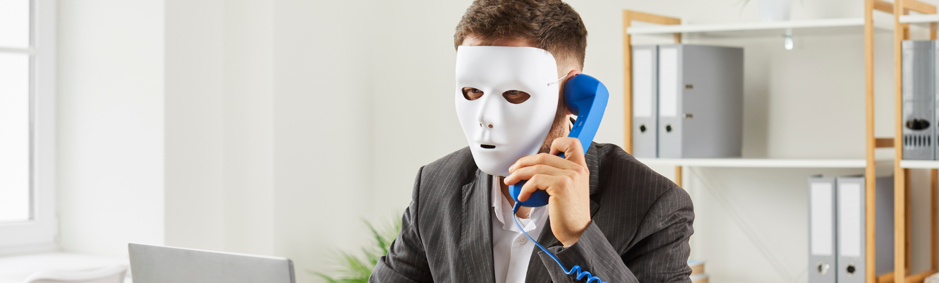 A professional wearing a white mask while speaking on a blue phone, symbolizing the concept of hiring scams and fraudulent activity on LinkedIn.